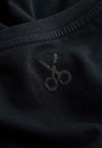 Zwart stof met een subtiele, getextureerde schaarlogo. De halslijn is rond met een gladde, gestikte rand.