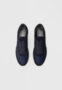 Ζευγάρι ναυτικό μπλε καθημερινά αθλητικά παπούτσια με μαύρα τρουκς και κορδόνια με λευκές λεπτομέρειες, εμφανιζόμενα από πάνω σε απλό ανοιχτό γκρι φόντο.