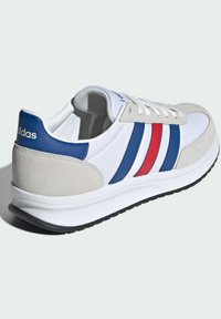 Baskets blanches avec des rayures bleues et rouges, tige en daim et synthétique, fermeture à lacets, semelle rembourrée, avec le logo 'cloudfoam' sur le côté.