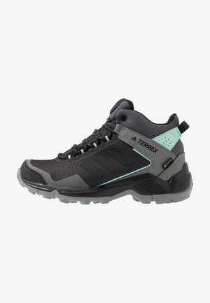 Chaussure de randonnée Adidas Terrex montante noire et grise avec des touches menthe, laçage à l'avant et semelle en caoutchouc texturée pour une bonne adhérence en extérieur.