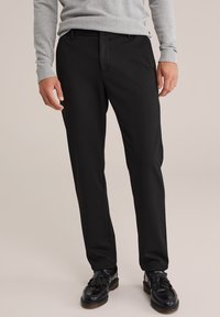 Svart skräddarsydda byxor i slätt tyg, med rak benmodell och framfickor. Bärs med svarta snörskor och en grå tröja.