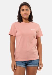 Lichtroze katoenen t-shirt met korte mouwen, ronde hals en een klein wit logo aan de linkerkant. Gecombineerd met spijkerbroekshorts.