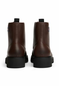 Braune Leder-Stiefeletten mit glatter Textur, kurzer Höhe, schwarzen Gummisohlen und einem Zugtab hinten. Mit einem Logo-Patch an der Seite.