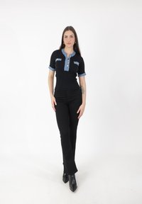 Czarna krótkoszlfowa bluzka z prążkowanej dzianiny z deninowym kołnierzykiem i akcentami kieszeni, z zapięciem na guziki. Noszona z czarnymi spódnicami w stylu dzwonów i botkami za kostkę.