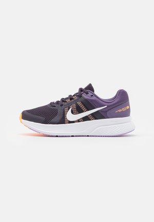 Zapato deportivo púrpura y negro con parte superior de malla, logo blanco de Nike, detalles en naranja y suela texturizada. Presenta un sistema de cordones destacado.
