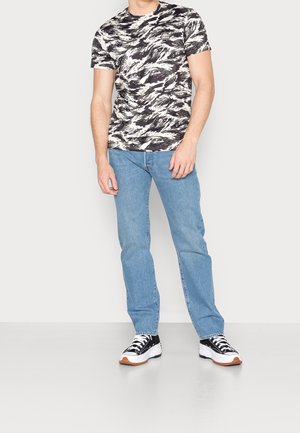 Svartvitt mönstrad t-shirt med korta ärmar, kombinerad med ljusblå jeans och svarta sneakers med vita och orange detaljer.