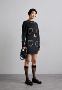 Cardigan negru din tricot cu detalii albe la buzunare, purtat peste o fustă neagră din tricot. Asortat cu loafers negri și ciorapi transparenți până la coapsă.