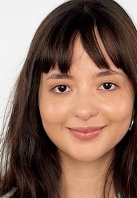 Zbliżenie na osobę z długimi, ciemnobrązowymi włosami i jasną skórą, o gładkiej teksturze i minimalnym makijażu, uśmiechającą się z subtelnymi dołeczkami.