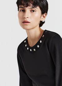 Schwarzes Oberteil mit rundem Ausschnitt, verziert mit silbernen, runden Nieten, langen Ärmeln und einer glatten Textur. Einfaches und modernes Design.