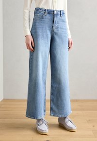 Bredde ben jeans i lys blå denim, med høy midje, frontlommer og rå kant, kombinert med grå semsket skinnsko.