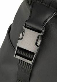 Czarna klamra plecaka z teksturowanym wykończeniem, wyposażona w metalowy zatrzask i taśmę parcianą. Gładkie materiały z subtelnymi akcentami przeszyć.