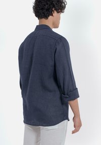 Navyblauwe linnen shirt met een ontspannen pasvorm, lange mouwen opgerold en een kraag. Soepele textuur en eenvoudige, strakke lijnen.