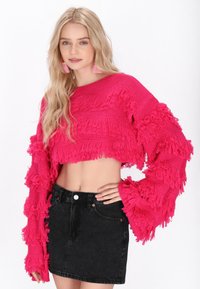 Roza skrajno odbito pulover s detajli fringa, dolgi rokavi in kontrasti tekstur, ujemajoč s temno črnimi jeans krilom visoke pasu.