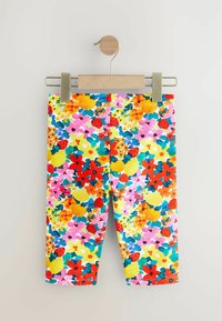 Színes leggings virágmintával, rózsaszín, sárga, piros és kék virágokkal fehér alapon. Pamut anyag, sima textúra.