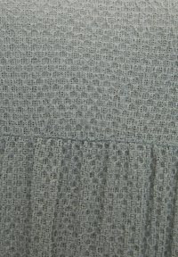 Tela texturizada de color gris claro con un diseño de encaje que presenta patrones circulares y volantes a lo largo del borde inferior, creando profundidad e interés visual.
