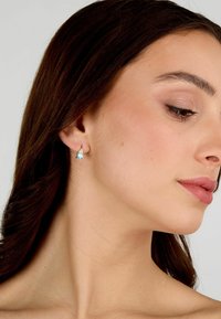 Orecchini dorati con una pietra azzurra a forma di pera. Il design è semplice ed elegante, adatto per diverse occasioni.