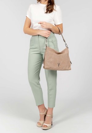 Sac à bandoulière beige texturé avec un dessus ouvert, des accessoires argentés et un logo discret. Le mannequin porte une chemise blanche, un pantalon vert clair et des escarpins crème.