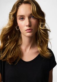 Fekete póló kerek nyakkivágással. A modell hullámos, vállig érő szőke hajú. A bőrszín természetesnek tűnik, minimális sminkkel.