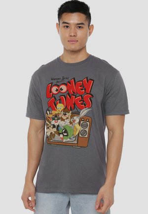 Young man wearing a gray Looney Tunes T-shirt featuring characters emerging from an old television set.