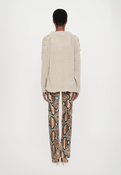 Beige knit sweater with gold buttons on shoulders, paired with snake-print trousers in brown and black tones. Smooth texture and relaxed fit.