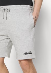 Sivé šortky s elastickým pásom vyrobené z jemnej česanej bavlny, s bočnými vreckami a čiernym logom "ellesse" na spodnej časti ľavej nohy.