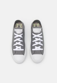 Para szarych trampek Converse All Star z białymi sznurówkami i gumowymi noskami widziana z góry na białym tle.