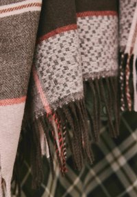 Wool scarf featuring brown and grey tones, a textured check pattern, and fringed edges with red and white accents.