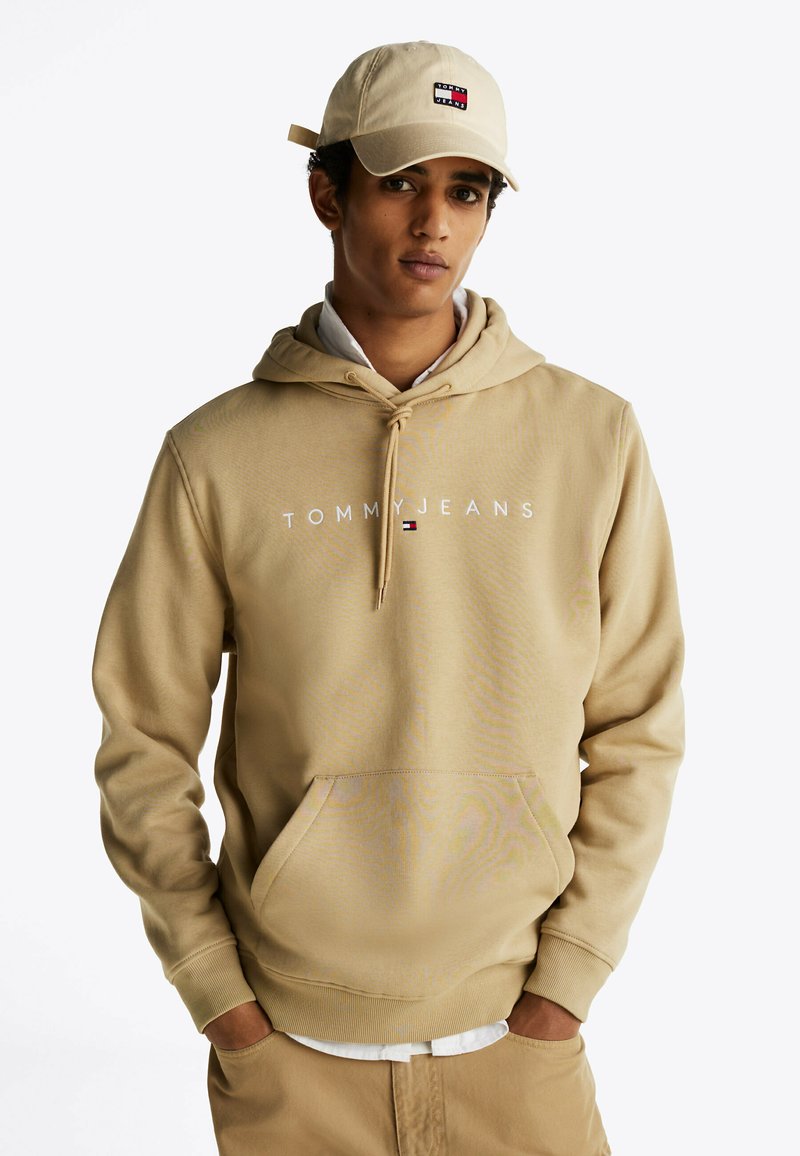 Beżowa bluza z kapturem z nadrukowanym logo "TOMMY JEANS", regulowanym sznurkiem i przednią kieszenią; zestawiona z beżową czapką z naszywką z logo.