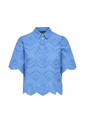 Blouse bleu clair à manches courtes avec bords festonnés, boutonnage frontal et détails de broderie florale ajourée sur le tissu.