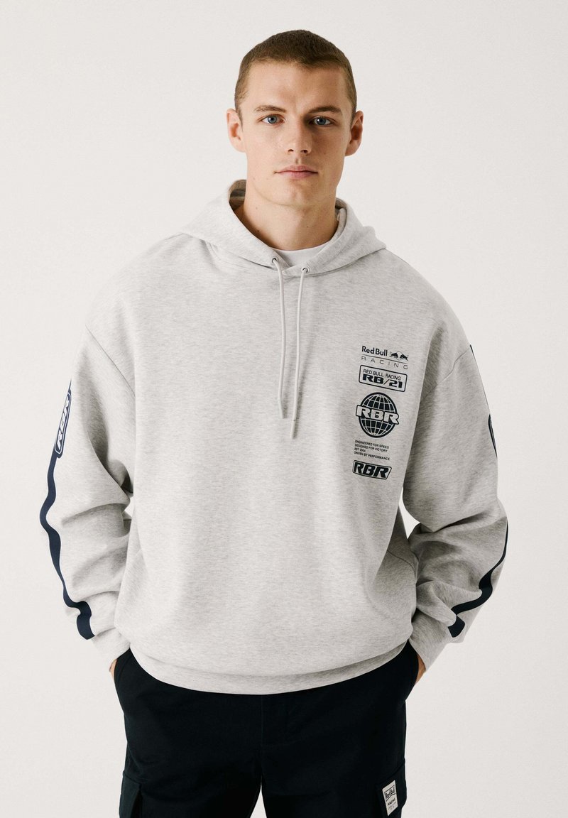 Sudadera gris claro con gráficos en el frente y las mangas, con capucha ajustable. Mangas largas con acentos en azul oscuro. Textura suave, ajuste casual.