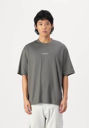 T-shirt gris à manches courtes avec encolure ronde et imprimé logo sur la poitrine. Fabriqué en coton doux avec une coupe surdimensionnée.