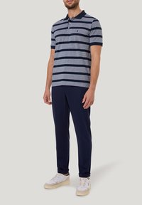 Kurzärmliges Polohemd in Marineblau mit grauen Streifen, ausgestattet mit einem Kragen und drei Knöpfen. Kombiniert mit Marineblauen Hosen und weißen Sneakern.