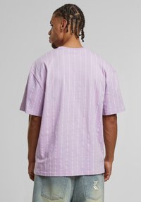 T-shirt en coton lilas à manches courtes et rayures verticales blanches, avec une coupe décontractée et un col rond.