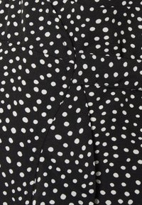 Černá tkanina s rozptýleným vzorem bílých puntíků, vyznačující se hladkou texturou a skládáním pro zvýšení rozměru.