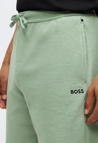 Niste joggeri verzi cu textură, cu talie cu șnur, buzunare laterale și un logo negru "BOSS" pe piciorul stâng.