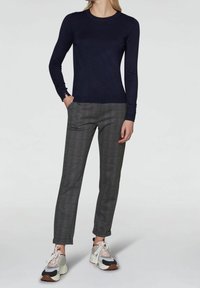 Femme portant un haut manches longues bleu marine, un pantalon slim à carreaux gris, et des baskets blanches épaisses avec des accents roses.
