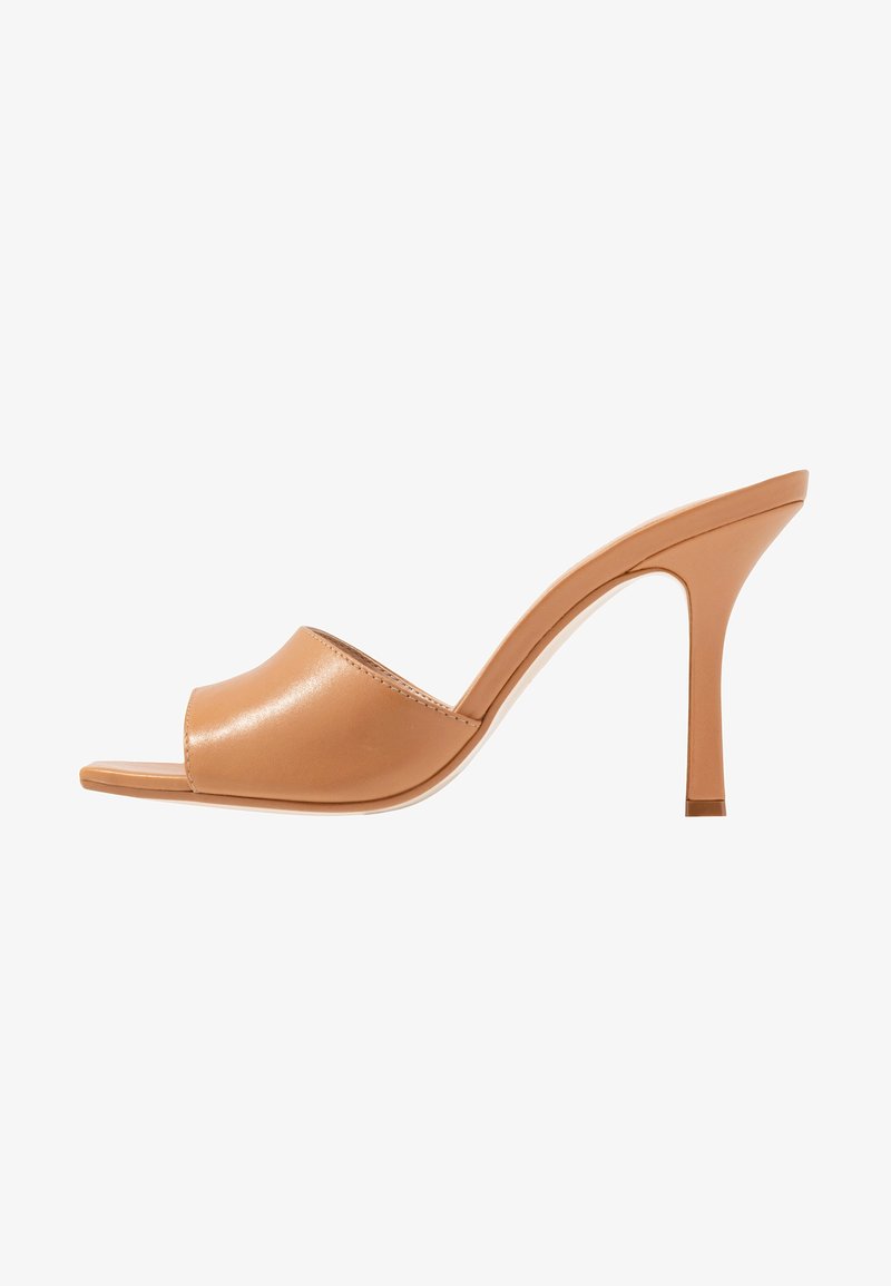 Sandales à talons synthétiques beiges avec un bout ouvert et une large bride. Le talon est fin et effilé, conçu pour une silhouette moderne.