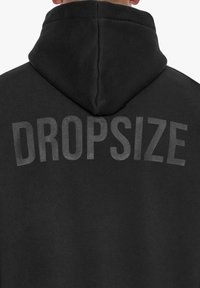 Schwarzer Hoodie mit einer vorderen Kängurutasche und einer Kapuze. "DROPSIZE" in fetten, leicht reflektierenden Buchstaben auf dem Rücken gedruckt. Glatte Textur.