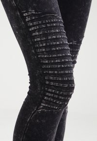 Čierne legíny vyrobené z elastického materiálu s poškodeným povrchom a vertikálnymi ryhami pozdĺž stehien.