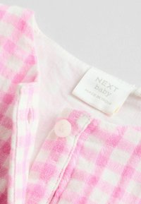 Rosa och vit rutigt tyg med en mjuk struktur, med en knappstängning och en etikett som läser "NEXT baby, MADE IN INDIA."