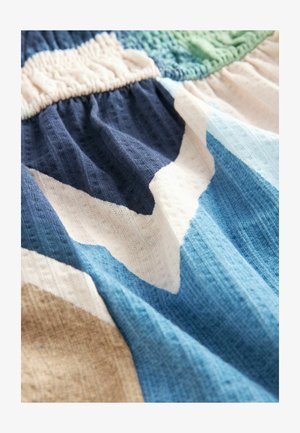 Geomeetrilise mustriga tekstiil, mis sisaldab sinise, tumesinise, kreemi ja beeži värve. Kangas on tekstuurse ja kudumisega välimusega ning sellel on ronkseest.