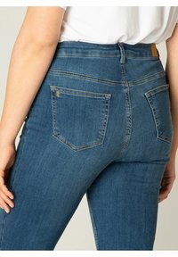 High-waisted blauwe spijkerbroeken van denim, met achterzakken met zichtbare stiksels en een getailleerd silhouet. Minimalistisch ontwerp.