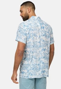 Camisa de algodón de manga corta con un estampado de paisajes en azul claro y blanco, con cuello clásico y corte relajado.