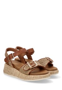 Sandalias de cuero marrón con acentos de paja trenzada, correas ajustables y detalles de hebillas, con una suela de esparto en forma de cuña.