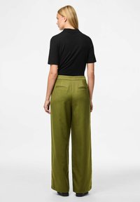 Zwart kortmouwtopje gecombineerd met olijfgroen high-waisted wijde broek met verticale strepen en achterzakken.