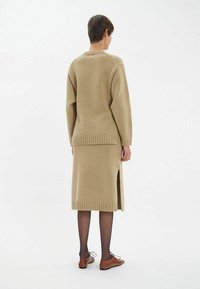 Ensemble en tricot beige composé d'un pull et d'une jupe assortis, avec un ourlet côtelé et une fente sur le côté. Porté avec des chaussures à lacets marron, montrant une texture de tissu.