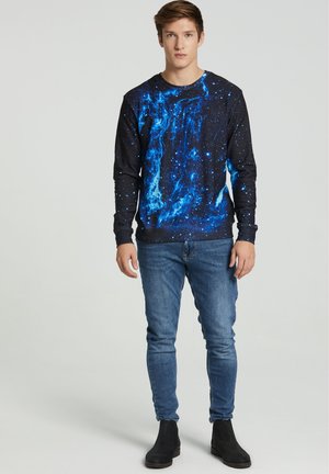 Sudadera negra con un estampado de galaxia azul, combinada con vaqueros ajustados de un azul claro y botas negras de tobillo. Textura de tela suave.