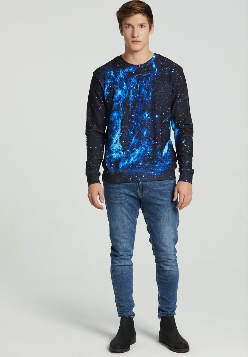 Black sweatshirt featuring a blue galaxy print, paired with light blue skinny jeans and black ankle boots. Smooth fabric texture.