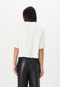 Hvit cropped bluse med korte ermer og krage, paret med svarte lærbukser. Glatt tekstur og rett snittdesign.