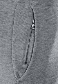 Close-up van een grijze gebreide stof met een gedeeltelijk open zilveren rits op een zak.